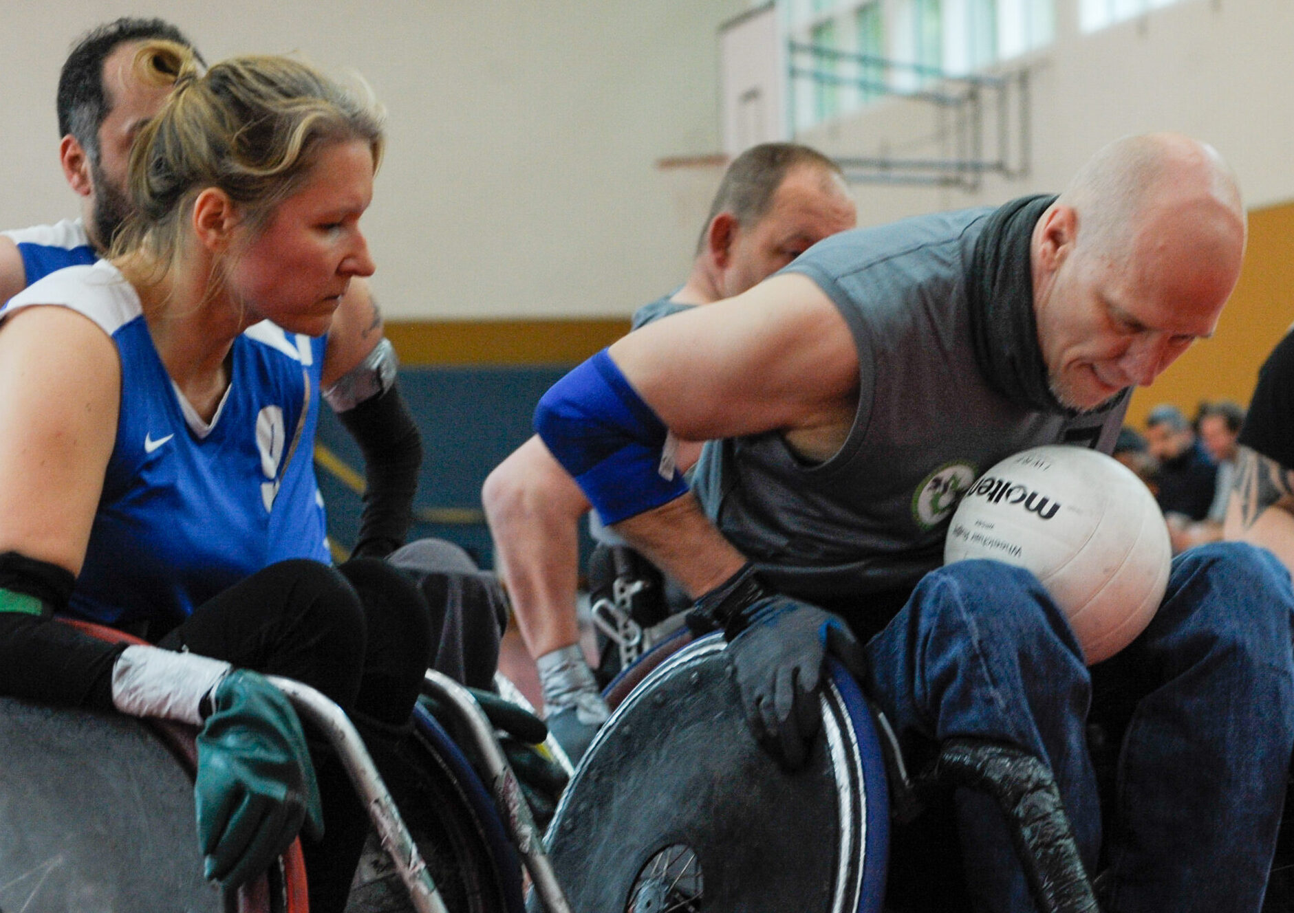 Duell zwischen einer Rollstuhlrugby-Splelerin und einem Rollstuhlrugby-Spieler. Der Mann ist imi Besitz des Spielballs und versucht, sich mit seinem Rugby-Stuhl über die Torlinie zu drücken. Die Spielerin blockt ihren Gegner mit ihrem Rugbystuhl.